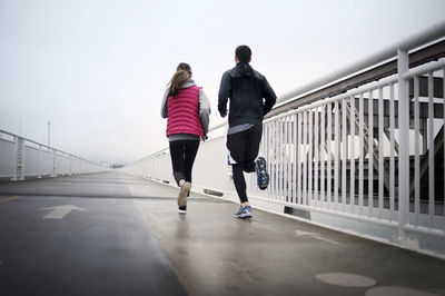 Rear view of athletes running on bay bridge against sky