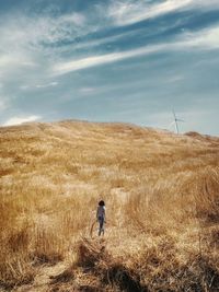 Woman walking on field against cloudy sky