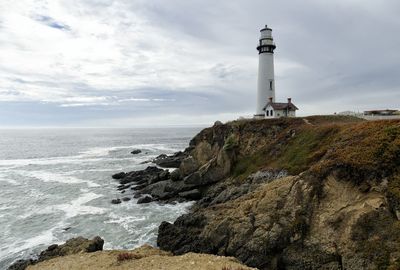 Lighthouse on beach by sea against sky