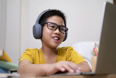 Smiling boy using laptop wearing headphone at home