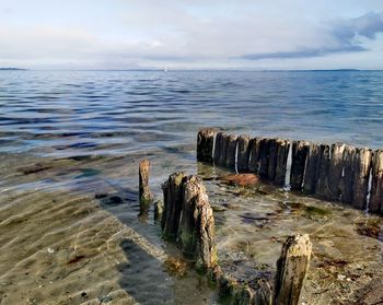 Wooden posts on beach by sea against sky