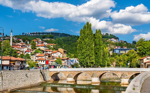 Arch bridge over river amidst buildings in town against sky