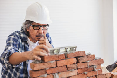 Mature man wearing hardhat making brick wall in workshop