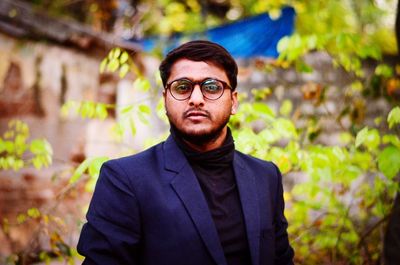 Portrait of young man in blazer standing against plants at yard