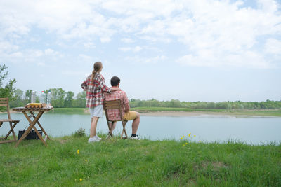 Rear view of woman standing by lake against sky