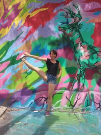 Full length of woman standing on one leg against graffiti wall