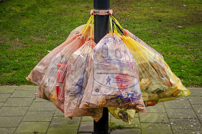 Bags of garbage attached to a lamppost on a sidewalk, waiting to be collected by municipal services
