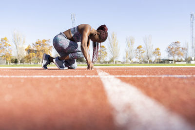 Female athlete in ready position on running track during sunny day