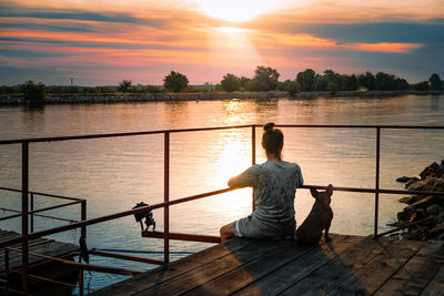 Man and french bulldog sitting on pier by danube river at sunset