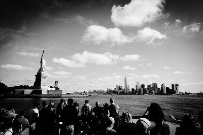 People looking at statue of liberty and manhattan against sky