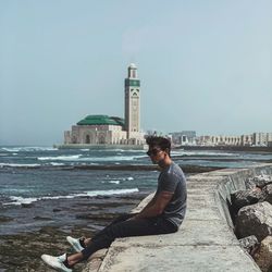 Man sitting on rock by sea against sky
