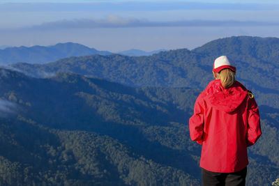 Rear view of young woman standing on mountain against blue sky