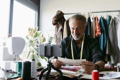 Smiling mature costume designer vlogging at work studio