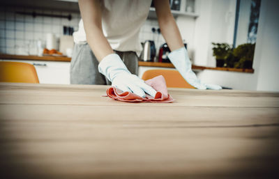 Midsection of woman cleaning wooden table at home
