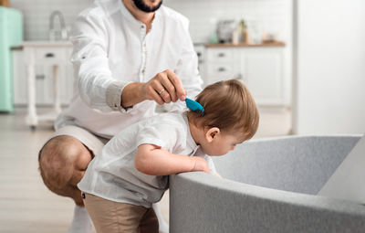 Dad uses a blue hair brush for a beautiful son while he plays