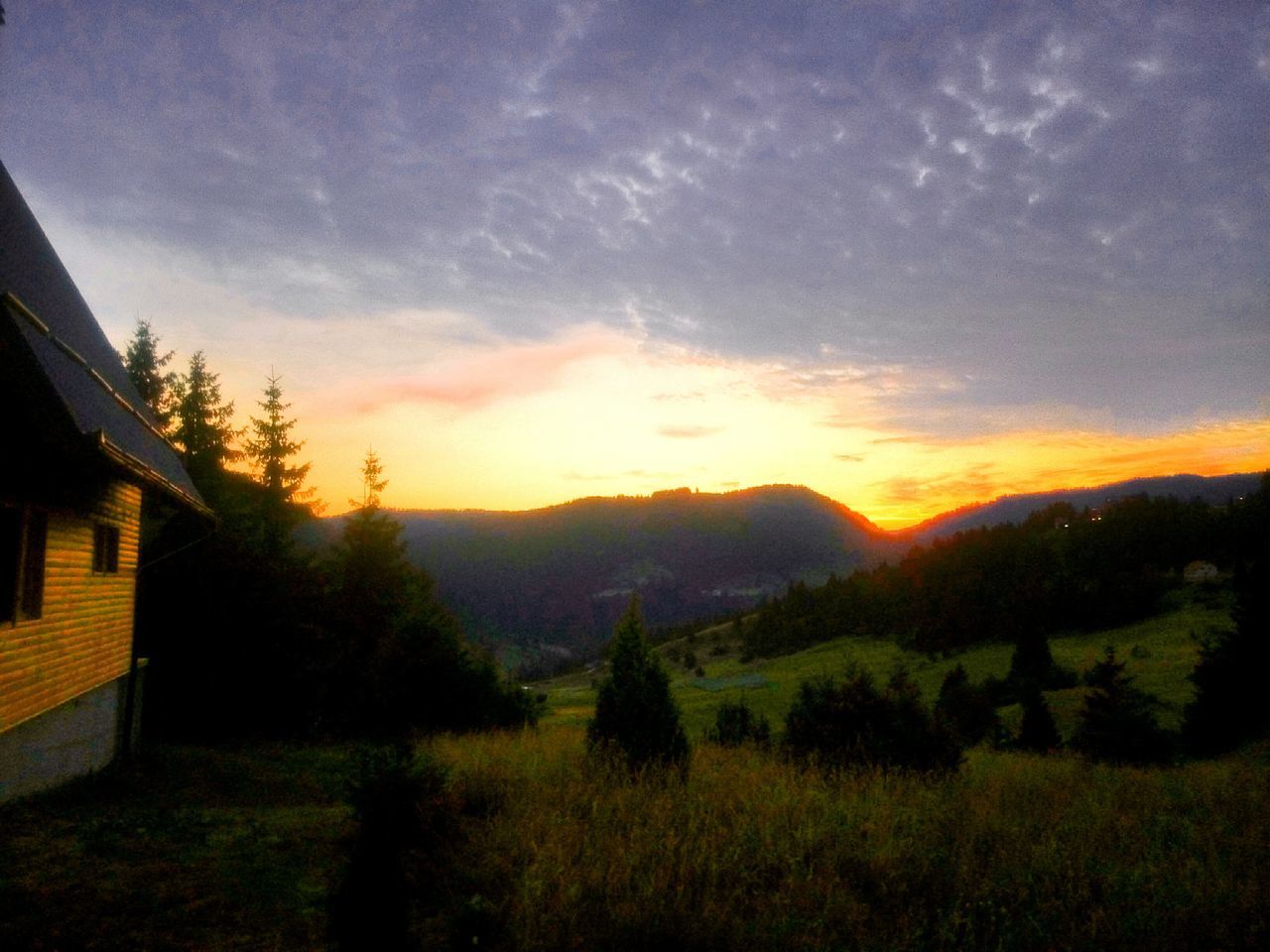 sunset, sky, landscape, beauty in nature, scenics, tranquil scene, building exterior, cloud - sky, tranquility, tree, field, house, nature, built structure, architecture, orange color, growth, mountain, cloud, idyllic