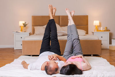 Couple lies on floor against background bed raised their legs and up, girl