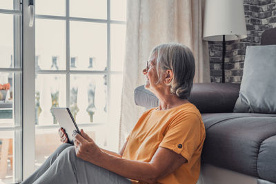 Side view of woman using digital tablet while sitting on sofa at home
