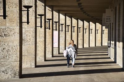 Rear view full length of sisters walking at colonnade on sunny day