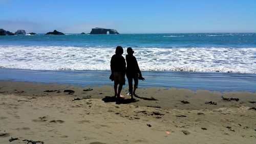 Rear view of man and woman standing at beach against sky