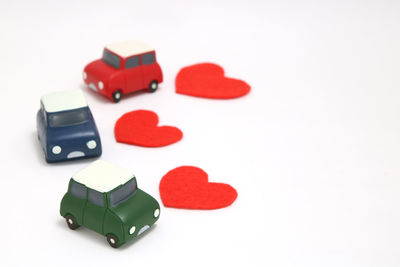 High angle view of multi colored toy cars and heart shapes over white background