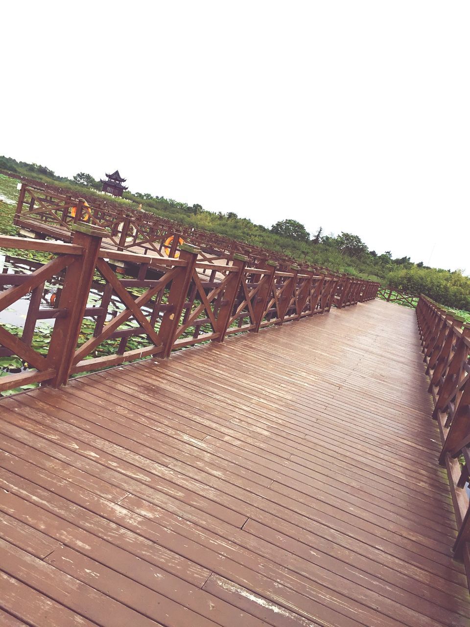 clear sky, wood - material, built structure, railing, copy space, tree, wooden, metal, sky, boardwalk, day, architecture, outdoors, pattern, no people, sunlight, fence, wood, low angle view, roof