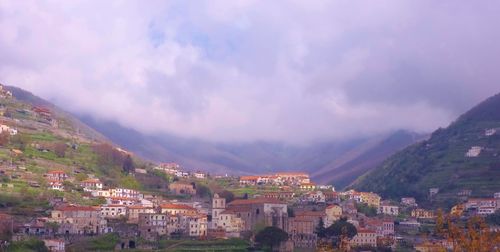 Village at valley against cloudy sky