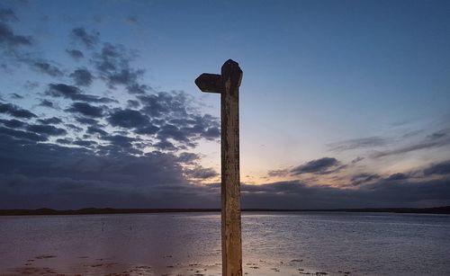 Silhouette wooden post on beach against sky during sunset
