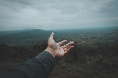 Midsection of person on landscape against cloudy sky