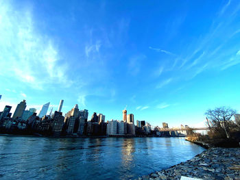 Buildings by river against blue sky