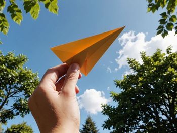 Low angle view of hand holding paper against sky