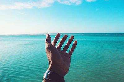 View of hand reaching towards sea