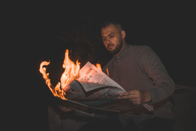 Young man holding burning newspaper at night