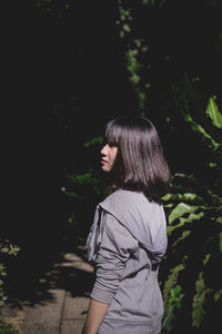 Young woman looking away while standing by plants