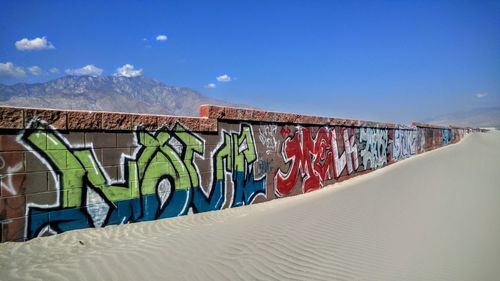 Colorful graffiti wall by sandy beach against sky