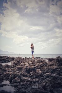 Rear view of woman standing on beach against sky