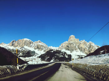 Road amidst snowcapped mountains against clear blue sky