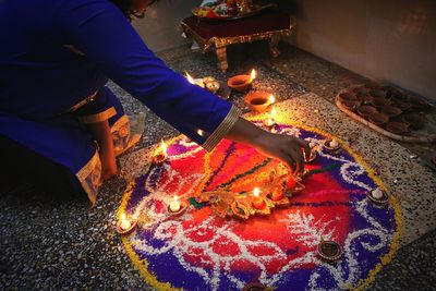 Midsection of woman decorating rangoli with candles on floor