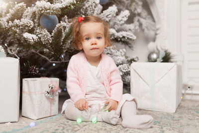 Portrait of cute baby girl sitting against christmas tree