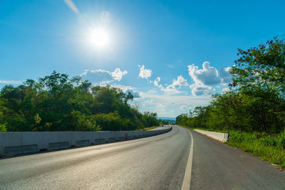 Road amidst trees against sky on sunny day