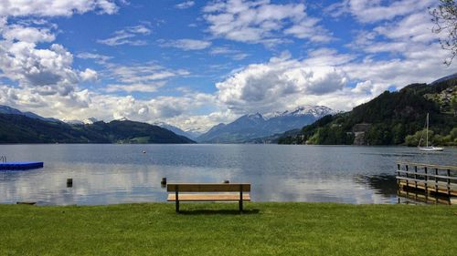 Bench by lake against sky
