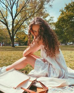 Low angle view of young woman sitting on field with curls