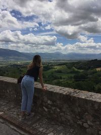 Rear view of woman standing on retaining wall against sky