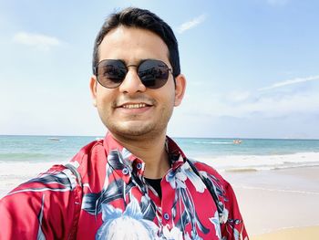 Portrait of smiling man wearing sunglasses at beach against sky