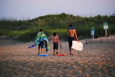 Rear view of men walking on beach against sky