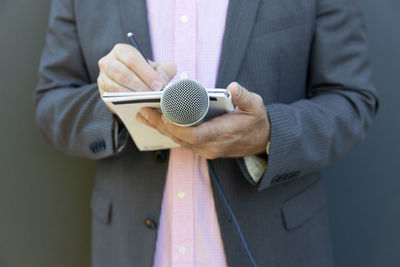 Midsection of man holding camera while standing against wall