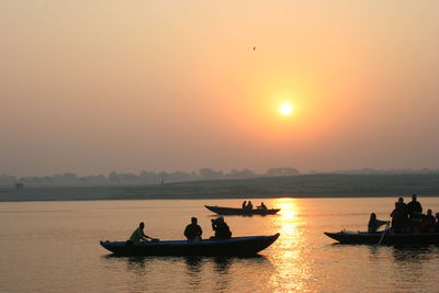 Silhouette people traveling in boat on sea against clear sky during sunset