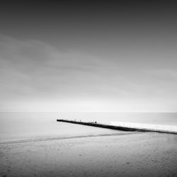 Pier at beach against sky during foggy weather