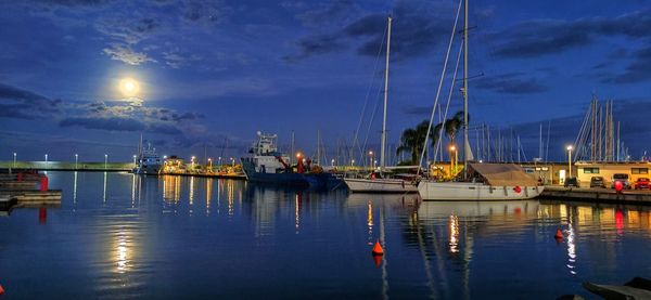 Boats moored in harbor at moonrise