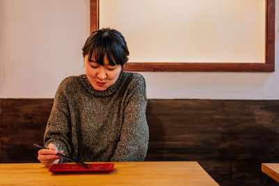 Young woman looking at camera while sitting on table